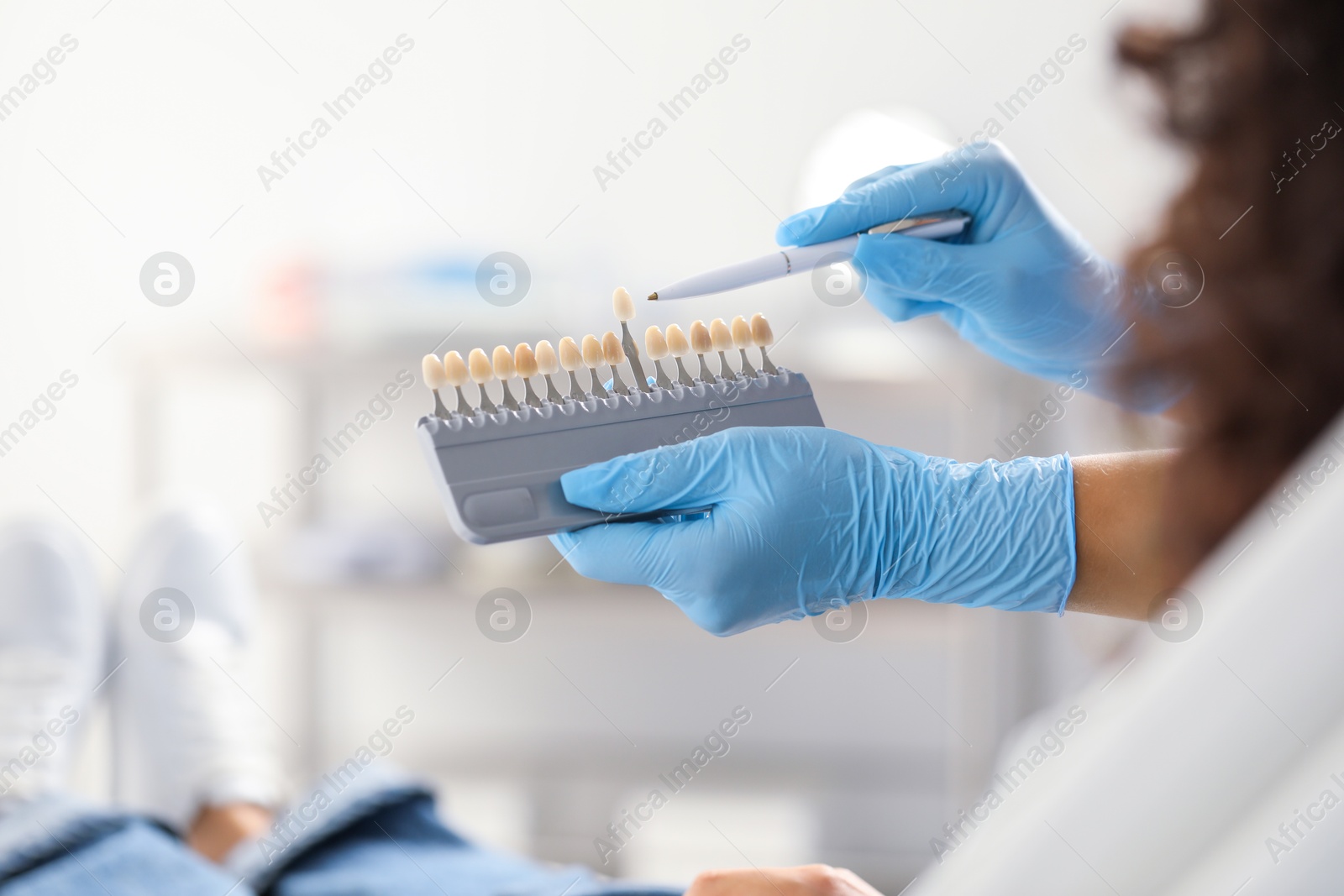 Photo of Doctor and patient choosing shade on teeth color palette in clinic, closeup. Dental veneers