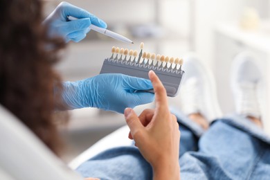 Photo of Doctor and patient choosing shade on teeth color palette in clinic, closeup. Dental veneers