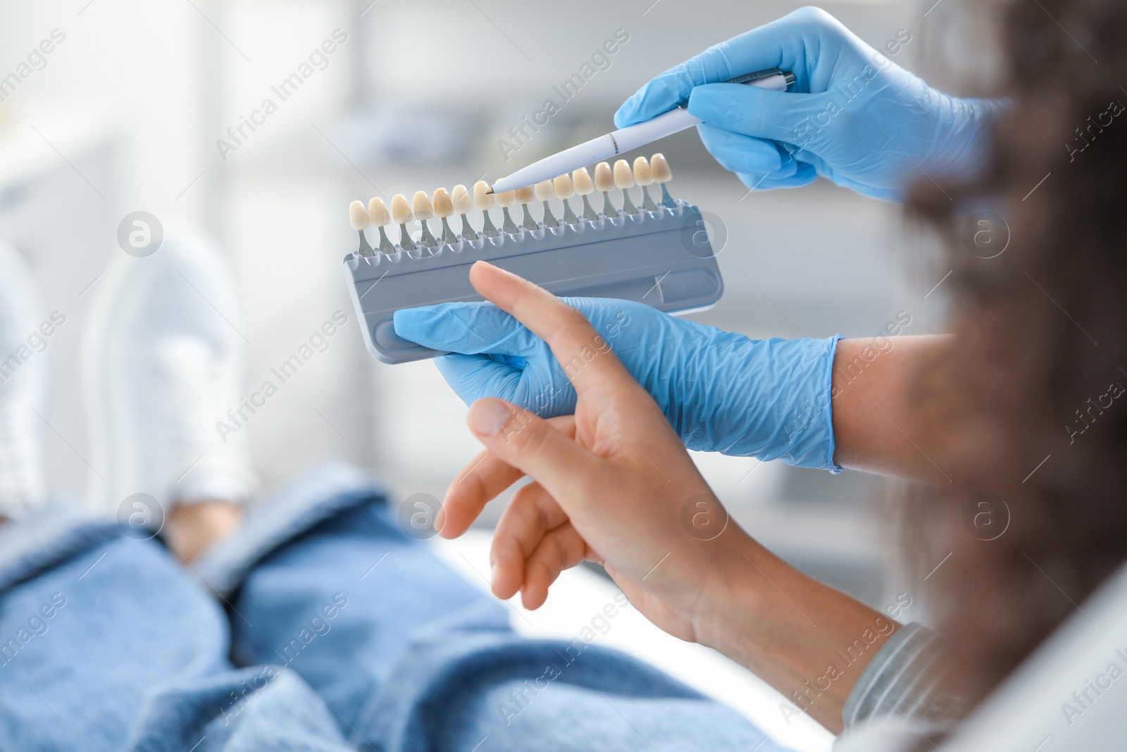 Photo of Doctor and patient choosing shade on teeth color palette in clinic, closeup. Dental veneers