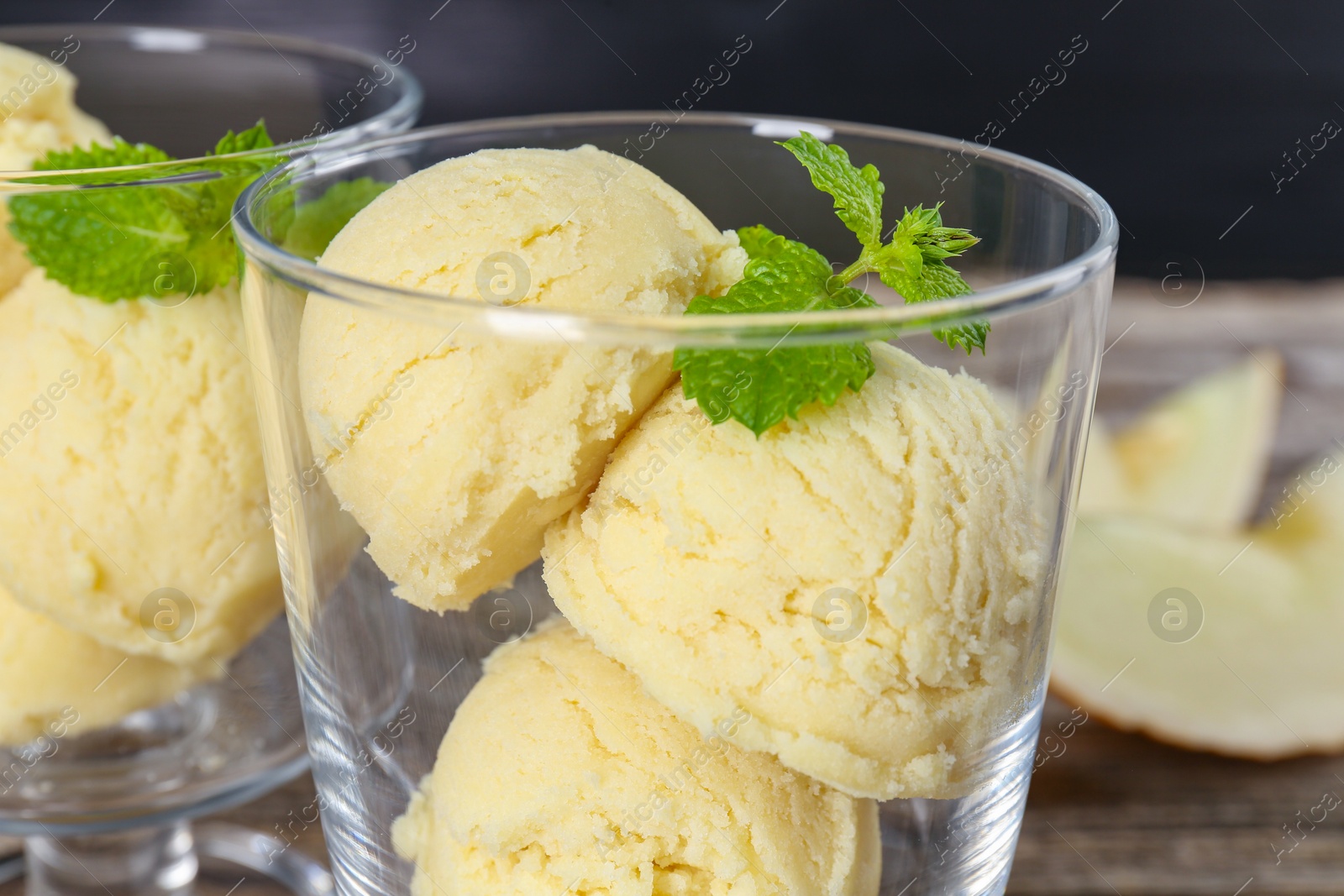 Photo of Scoops of melon sorbet and mint in glass dessert bowls on table, closeup