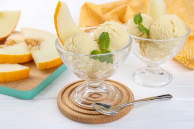 Photo of Scoops of melon sorbet with mint in glass dessert bowls and spoon on white wooden table, closeup