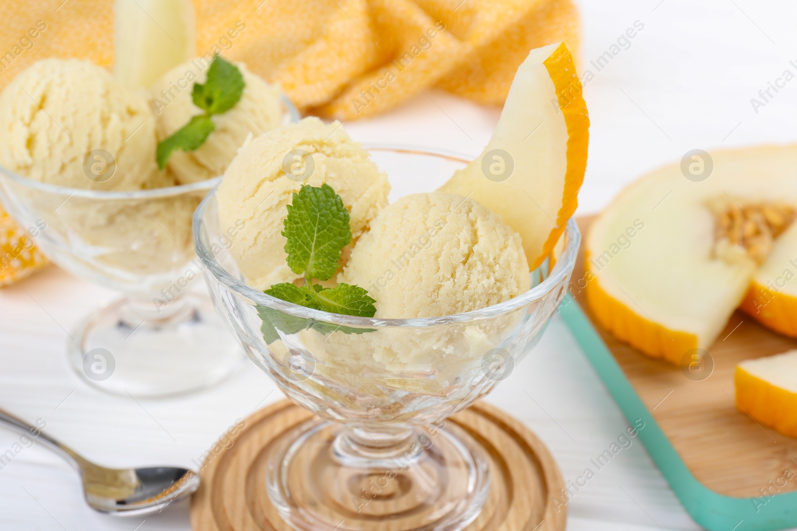 Photo of Scoops of melon sorbet with mint in glass dessert bowls and spoon on white table, closeup