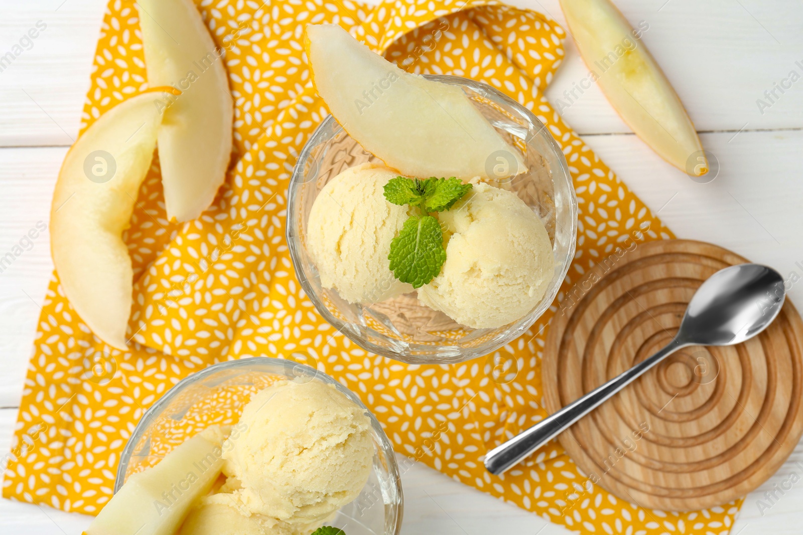 Photo of Scoops of melon sorbet with mint in glass dessert bowls, fresh fruit and spoon on white wooden table, flat lay