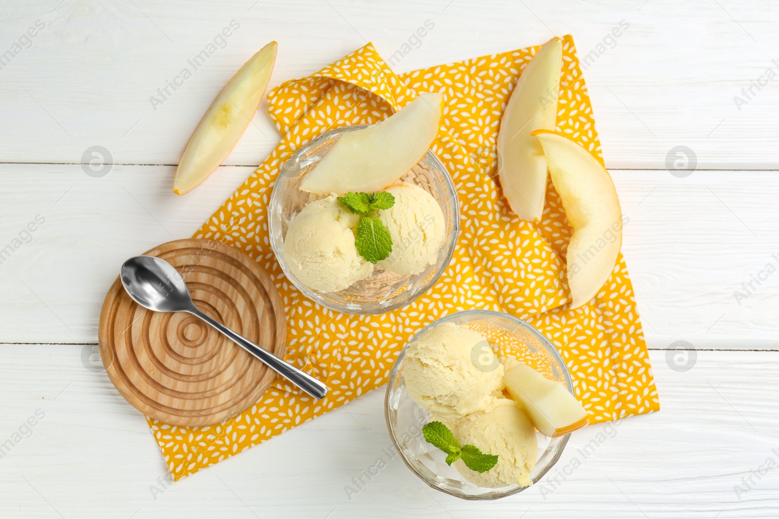 Photo of Scoops of melon sorbet with mint in glass dessert bowls, fresh fruit and spoon on white wooden table, flat lay