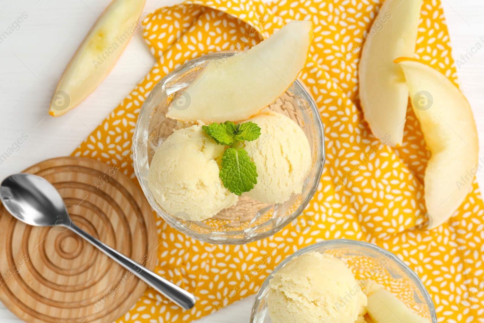 Photo of Scoops of melon sorbet with mint in glass dessert bowls, fresh fruit and spoon on white wooden table, flat lay