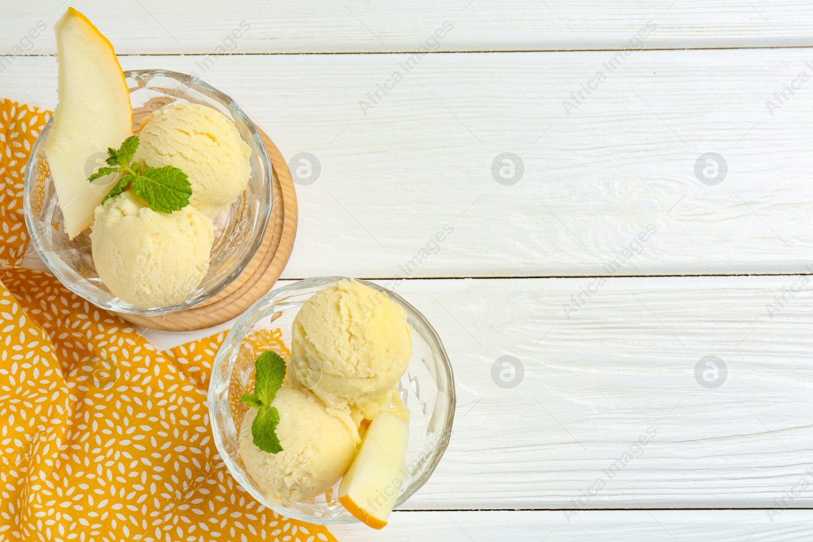 Photo of Scoops of melon sorbet with mint and fresh fruit in glass dessert bowls on white wooden table, top view. Space for text