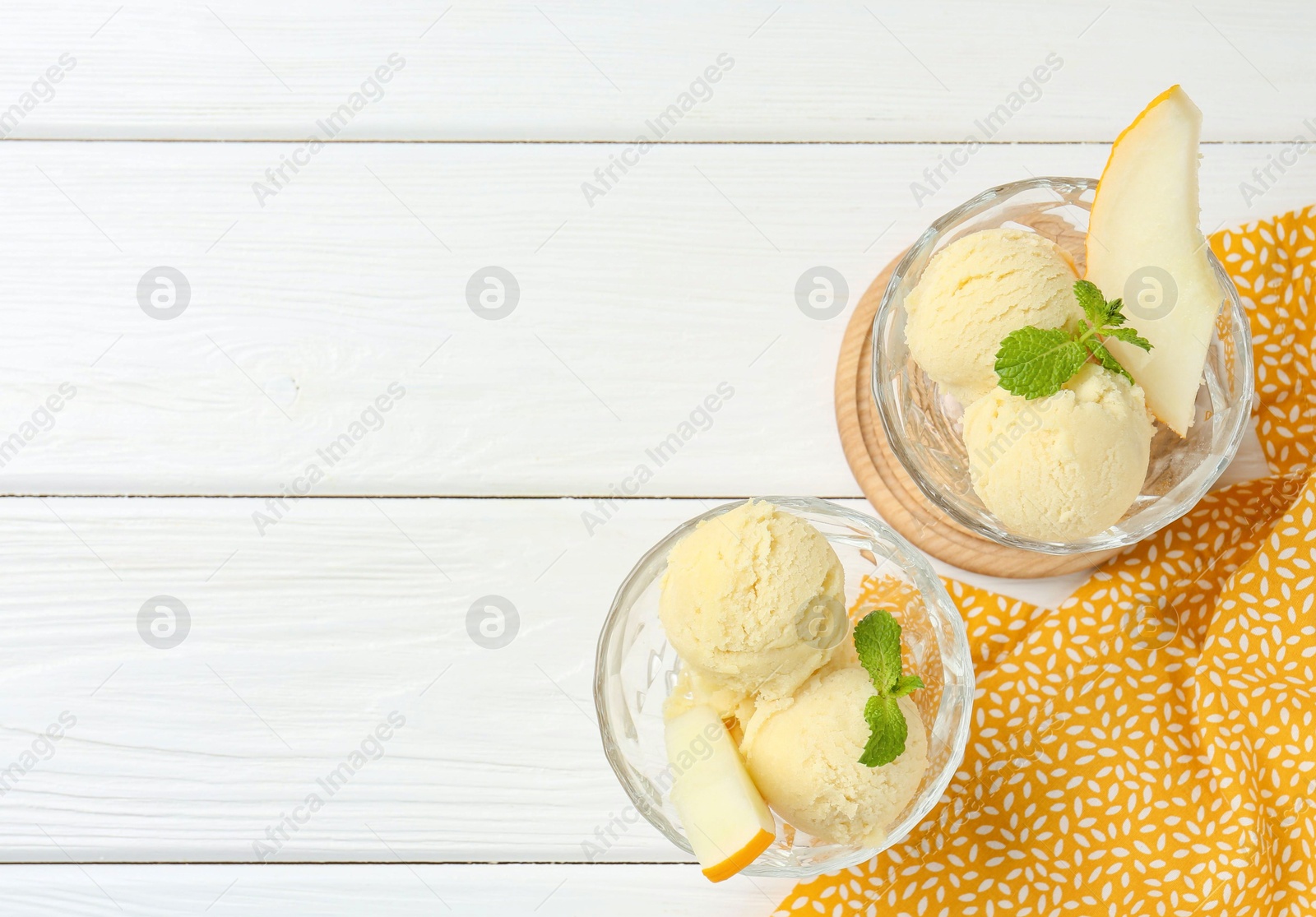 Photo of Scoops of melon sorbet with mint and fresh fruit in glass dessert bowls on white wooden table, top view. Space for text