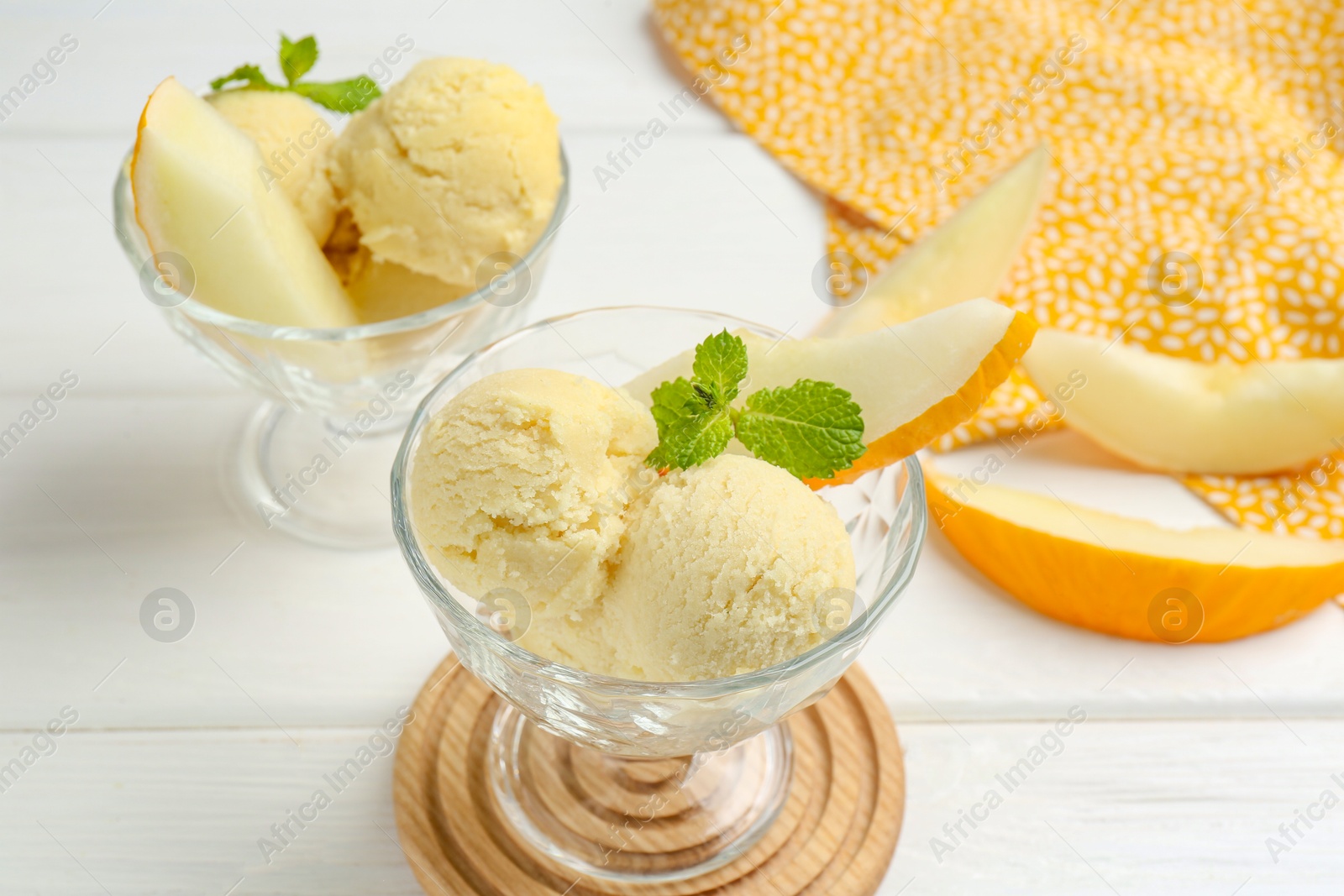 Photo of Scoops of melon sorbet with mint and fresh fruit in glass dessert bowls on white wooden table, closeup