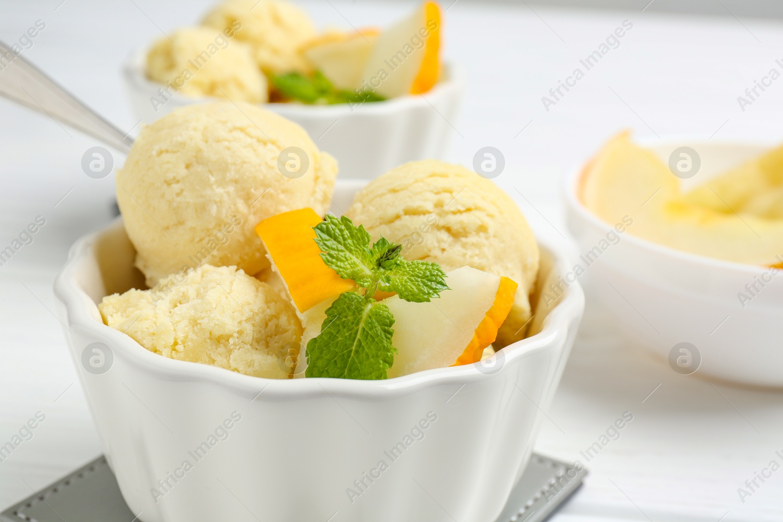 Photo of Scoops of melon sorbet with mint and fresh fruit in bowls on white table, closeup