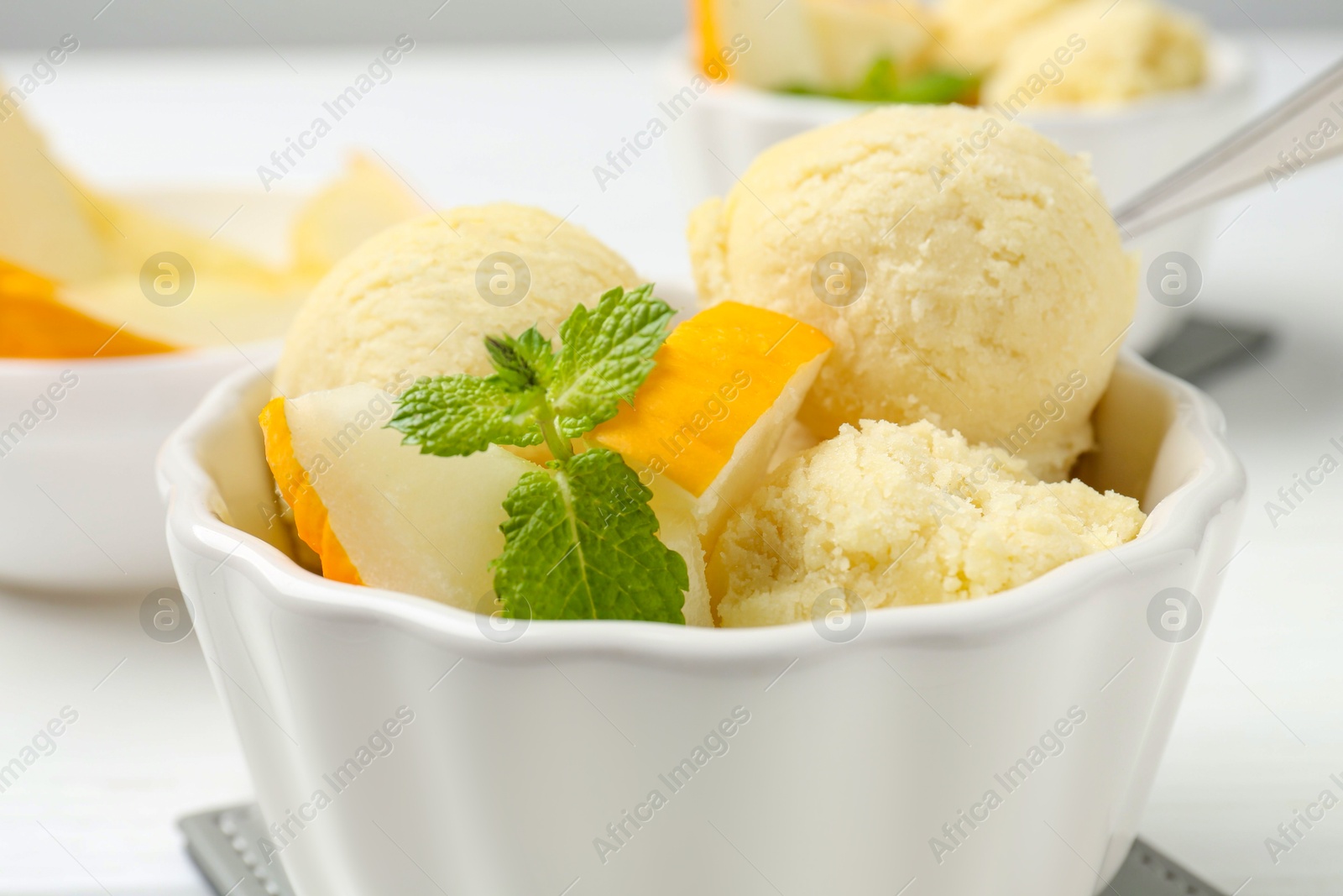 Photo of Scoops of melon sorbet with mint and fresh fruit in bowl on white table, closeup