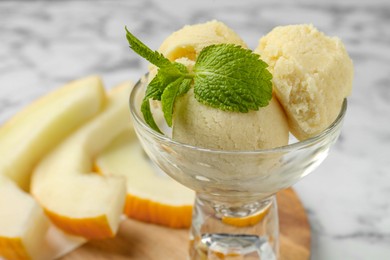 Photo of Scoops of melon sorbet with mint in glass dessert bowl and fresh fruit on light table, closeup