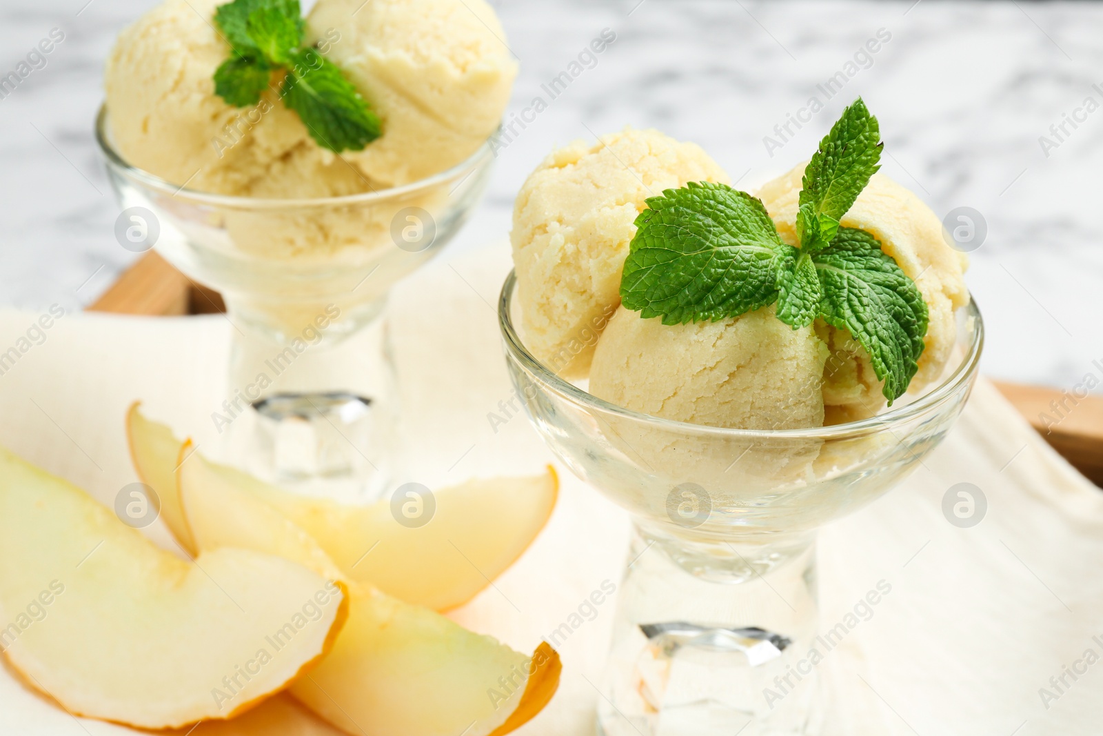 Photo of Scoops of melon sorbet with mint in glass dessert bowls and fresh fruit on light table, closeup