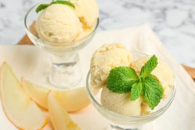 Photo of Scoops of melon sorbet with mint in glass dessert bowls and fresh fruit on light table, closeup