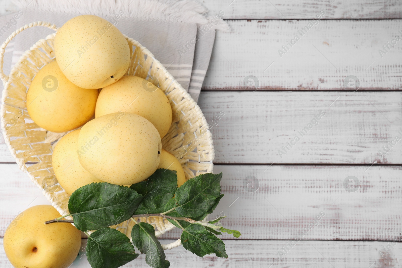 Photo of Delicious fresh apple pears in wicker basket and green leaves on white wooden table, top view. Space for text