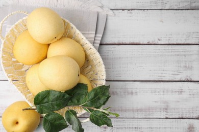 Photo of Delicious fresh apple pears in wicker basket and green leaves on white wooden table, top view. Space for text