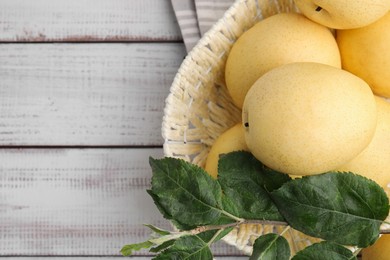 Photo of Delicious fresh apple pears in wicker basket and green leaves on white wooden table, top view. Space for text