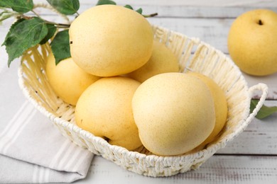 Photo of Delicious fresh apple pears in wicker basket and green leaves on white wooden table, closeup