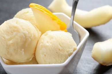 Photo of Scoops of tasty melon sorbet with fresh fruit and spoon in bowl on grey table, closeup