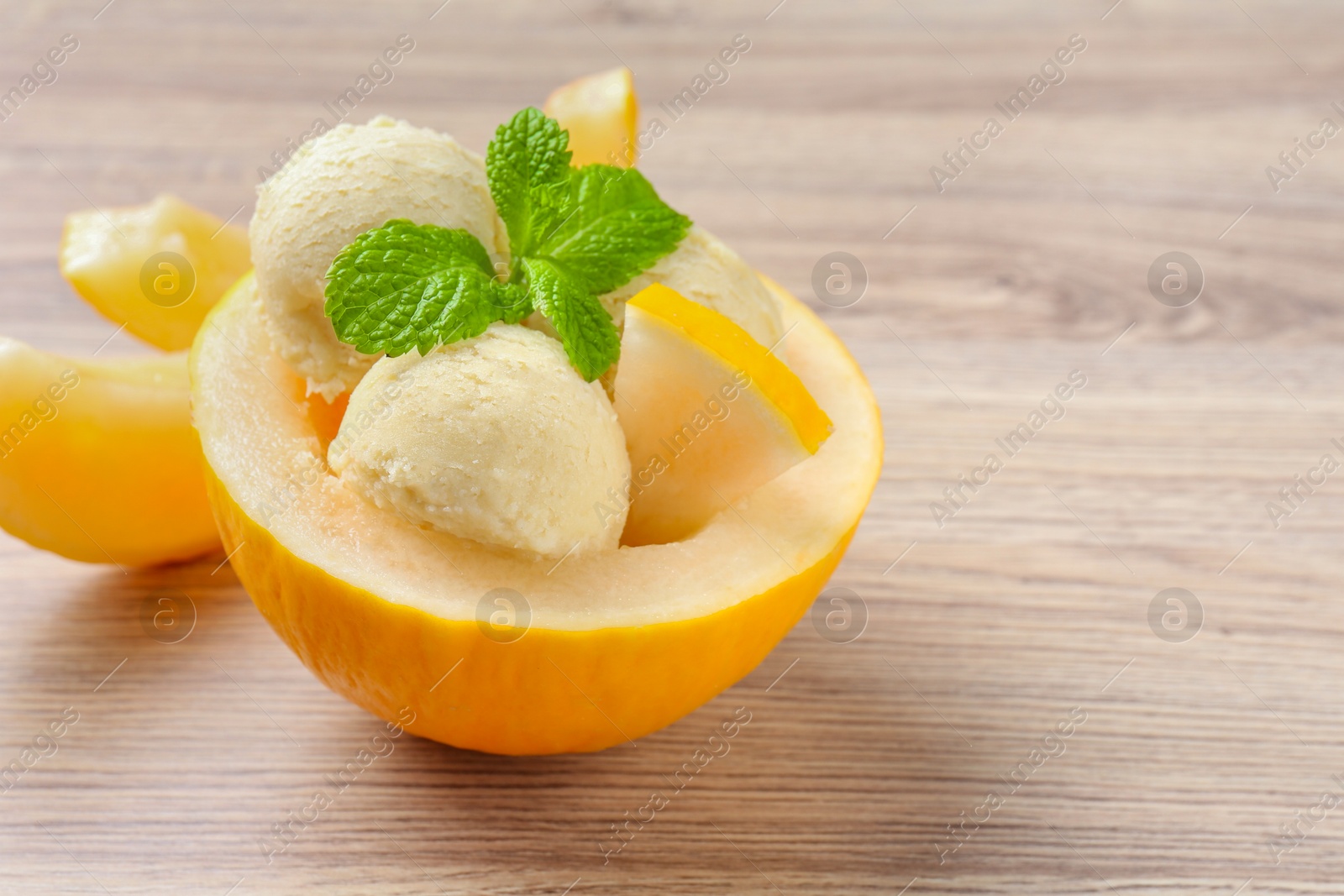 Photo of Scoops of tasty melon sorbet with mint in fresh fruit on wooden table, closeup. Space for text