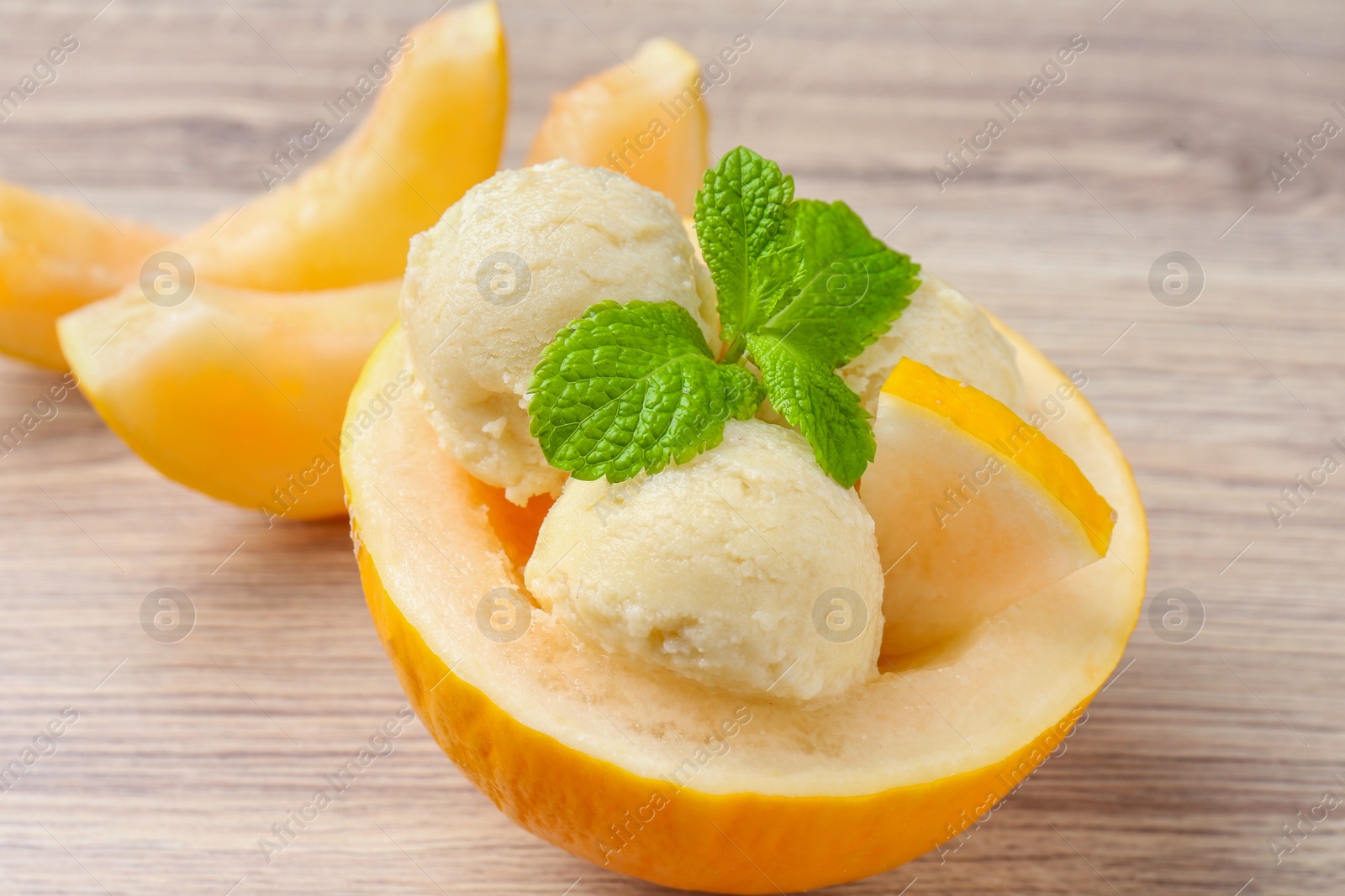 Photo of Scoops of tasty melon sorbet with mint in fresh fruit on wooden table, closeup