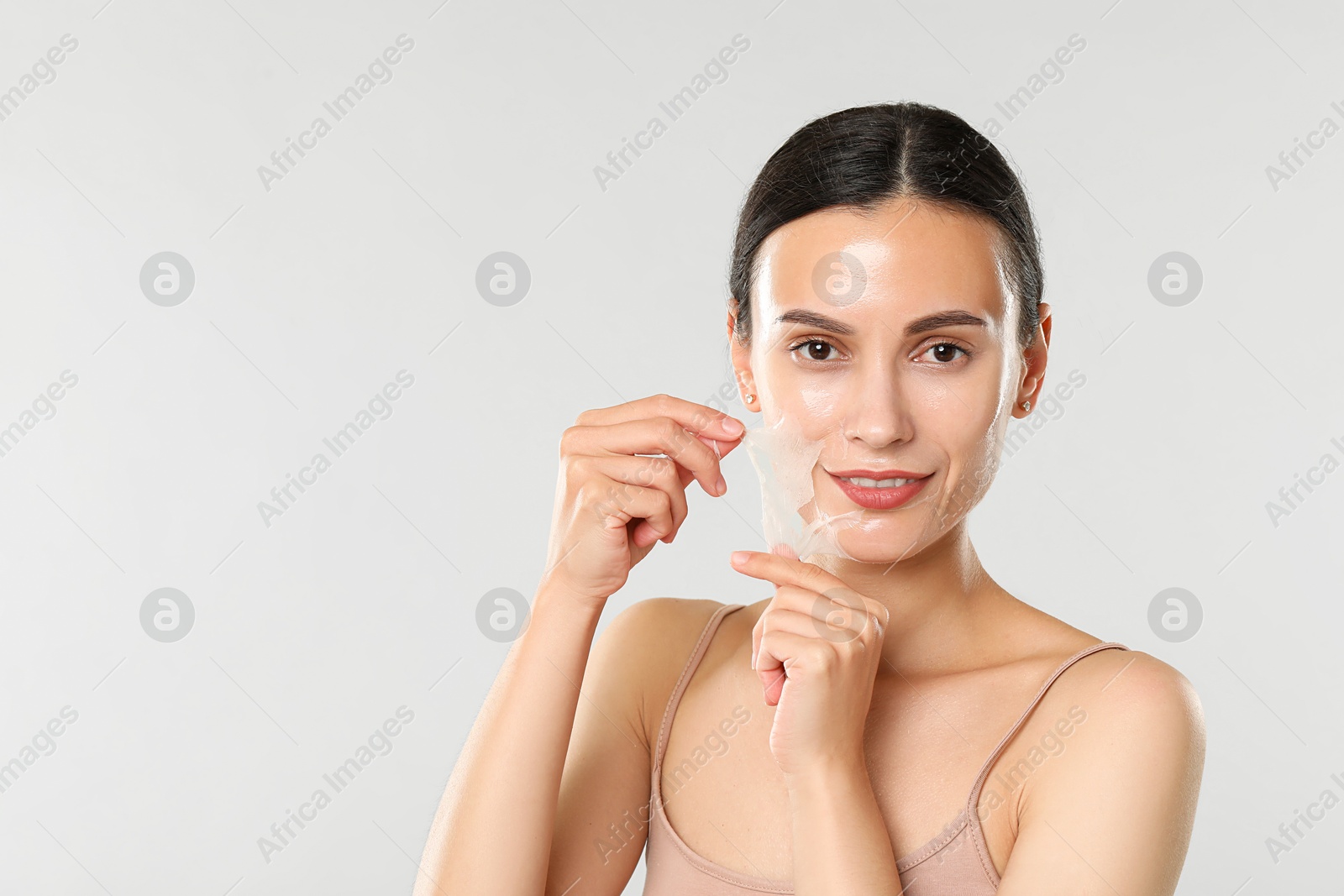 Photo of Smiling woman peeling off face mask on light grey background. Space for text