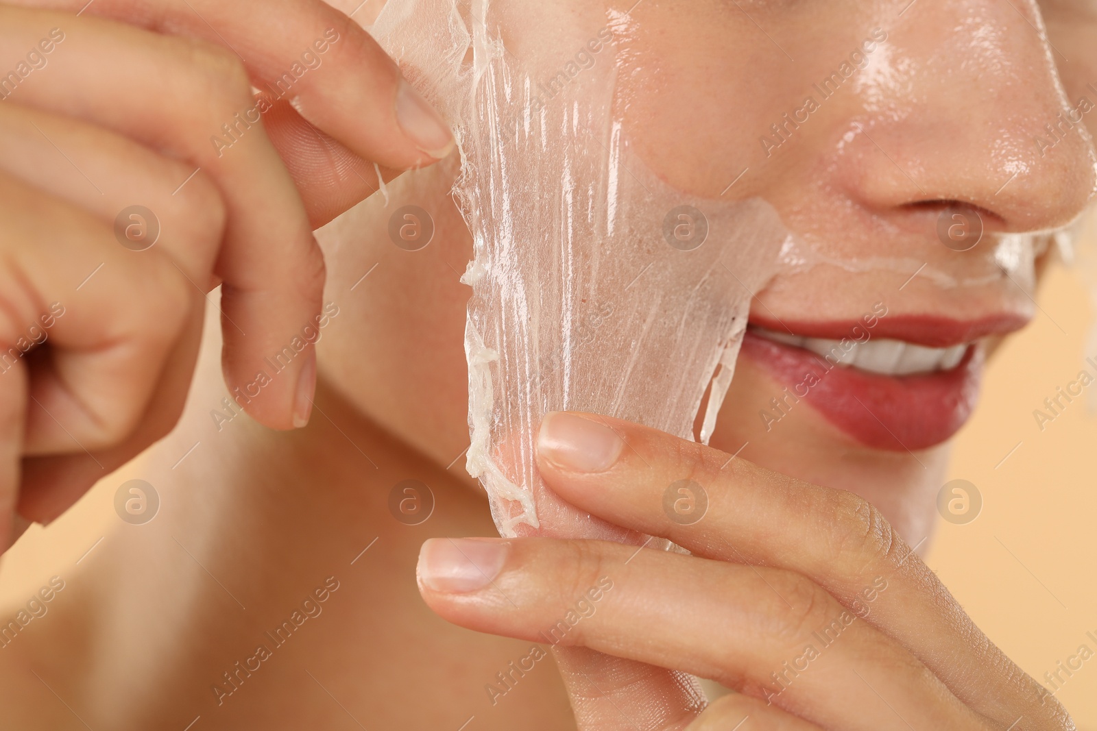 Photo of Woman peeling off face mask on beige background, closeup