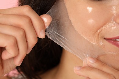 Photo of Woman peeling off face mask on pink background, closeup