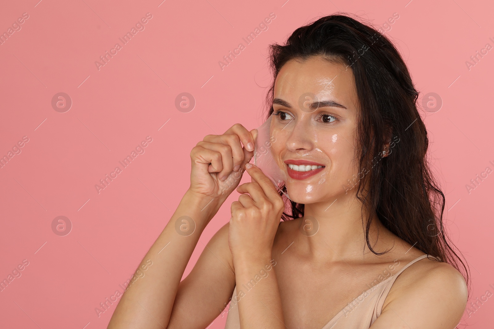 Photo of Smiling woman peeling off face mask on pink background. Space for text