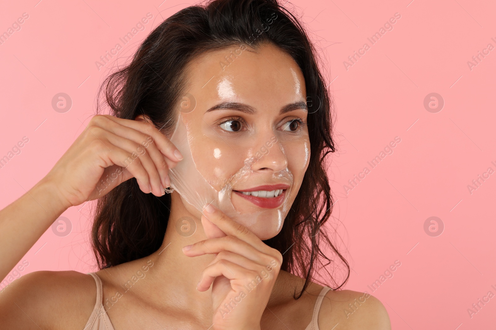 Photo of Smiling woman peeling off face mask on pink background