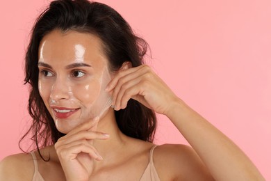 Photo of Smiling woman peeling off face mask on pink background