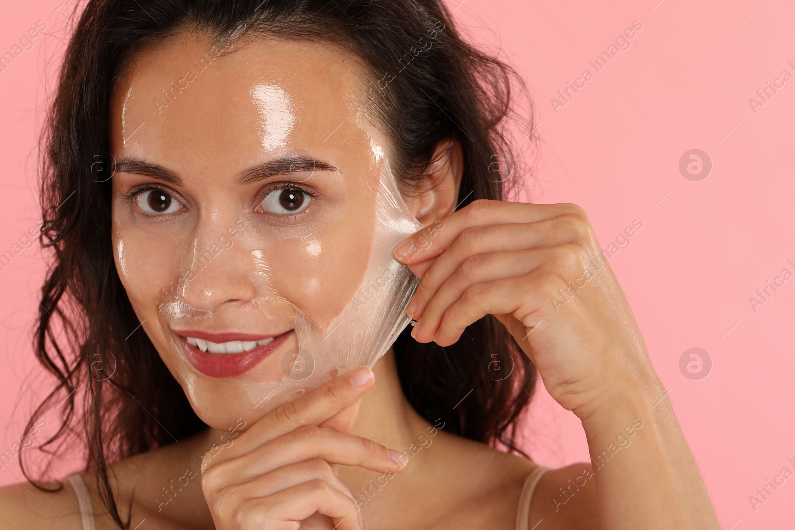 Photo of Smiling woman peeling off face mask on pink background