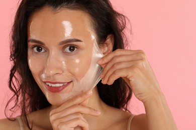 Photo of Smiling woman peeling off face mask on pink background