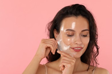 Photo of Smiling woman peeling off face mask on pink background. Space for text