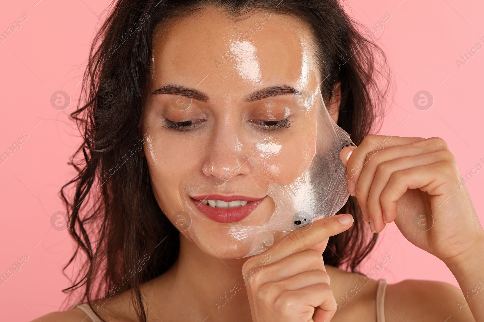 Photo of Smiling woman peeling off face mask on pink background, closeup