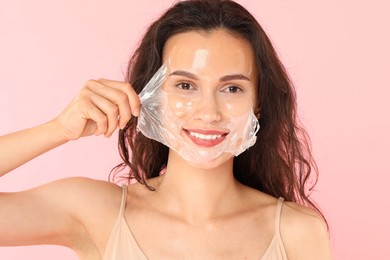 Smiling woman peeling off face mask on pink background