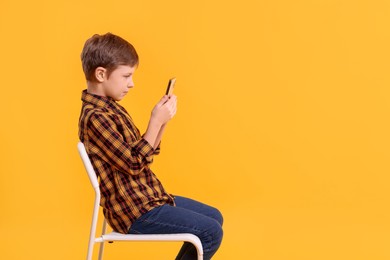 Photo of Boy with correct posture and smartphone sitting on chair against yellow background