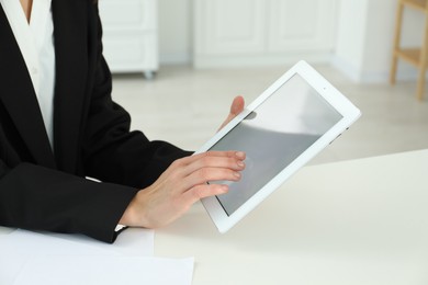 Photo of Businesswoman using tablet at white table indoors, closeup. Modern technology