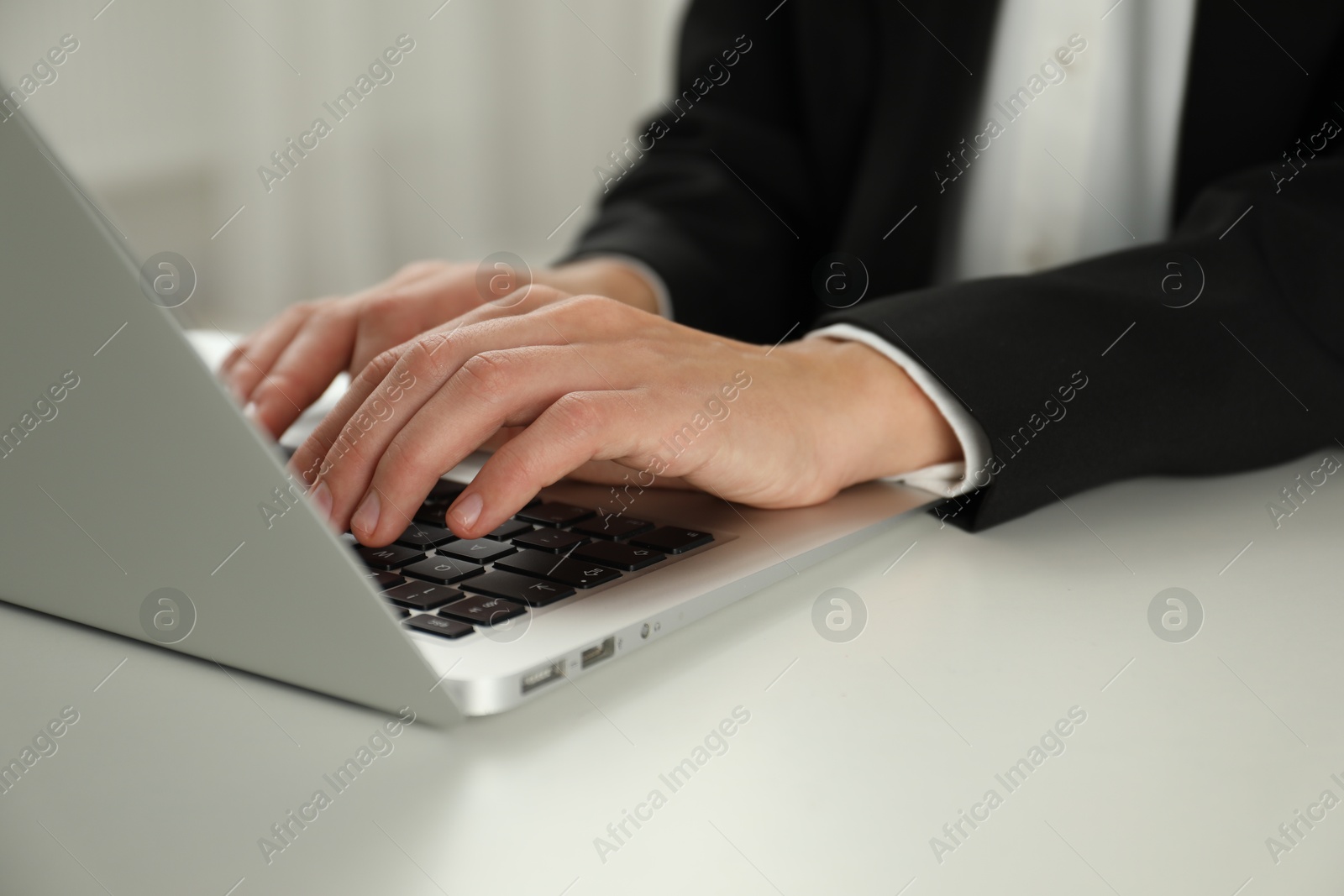 Photo of Businesswoman using laptop at white table indoors, closeup. Modern technology