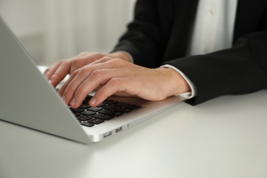 Photo of Businesswoman using laptop at white table indoors, closeup. Modern technology