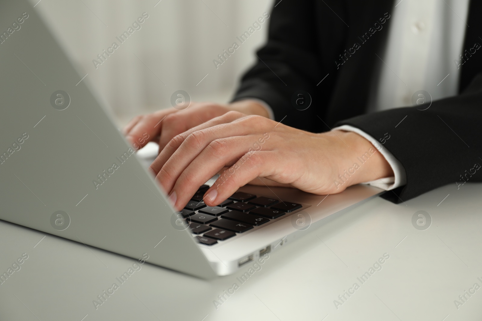 Photo of Businesswoman using laptop at white table indoors, closeup. Modern technology