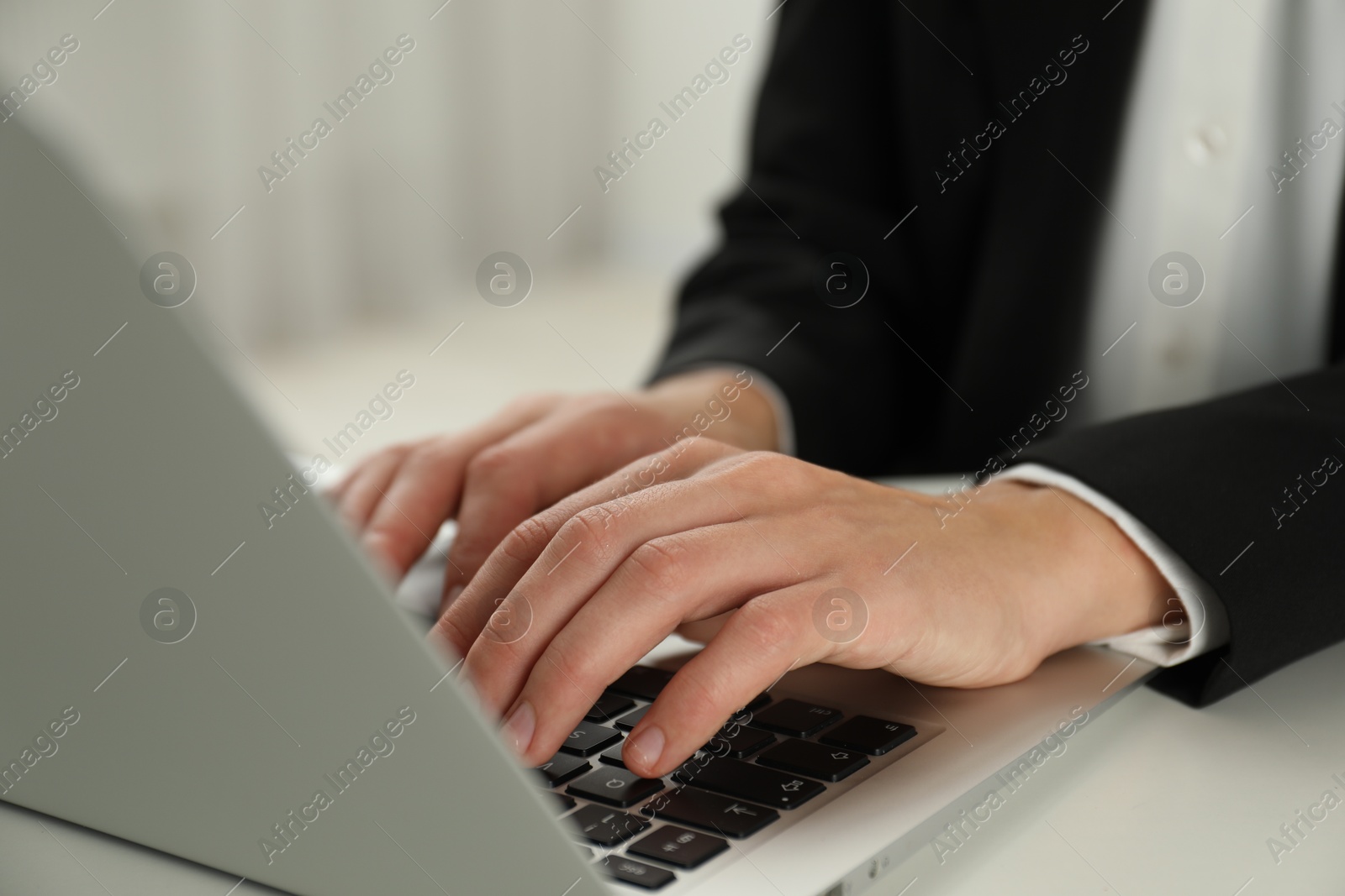 Photo of Businesswoman using laptop at white table indoors, closeup. Modern technology