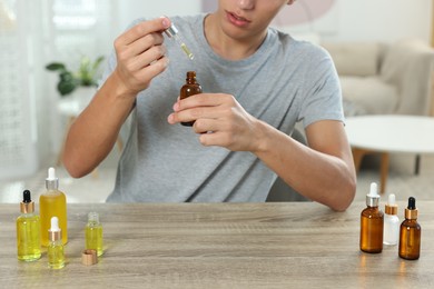 Photo of Young man dripping CBD tincture into bottle from dropper at wooden table, closeup