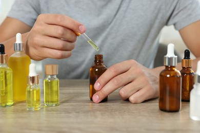 Photo of Young man dripping CBD tincture into bottle from dropper at wooden table, closeup