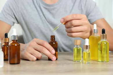 Photo of Young man dripping CBD tincture into bottle from dropper at wooden table, closeup