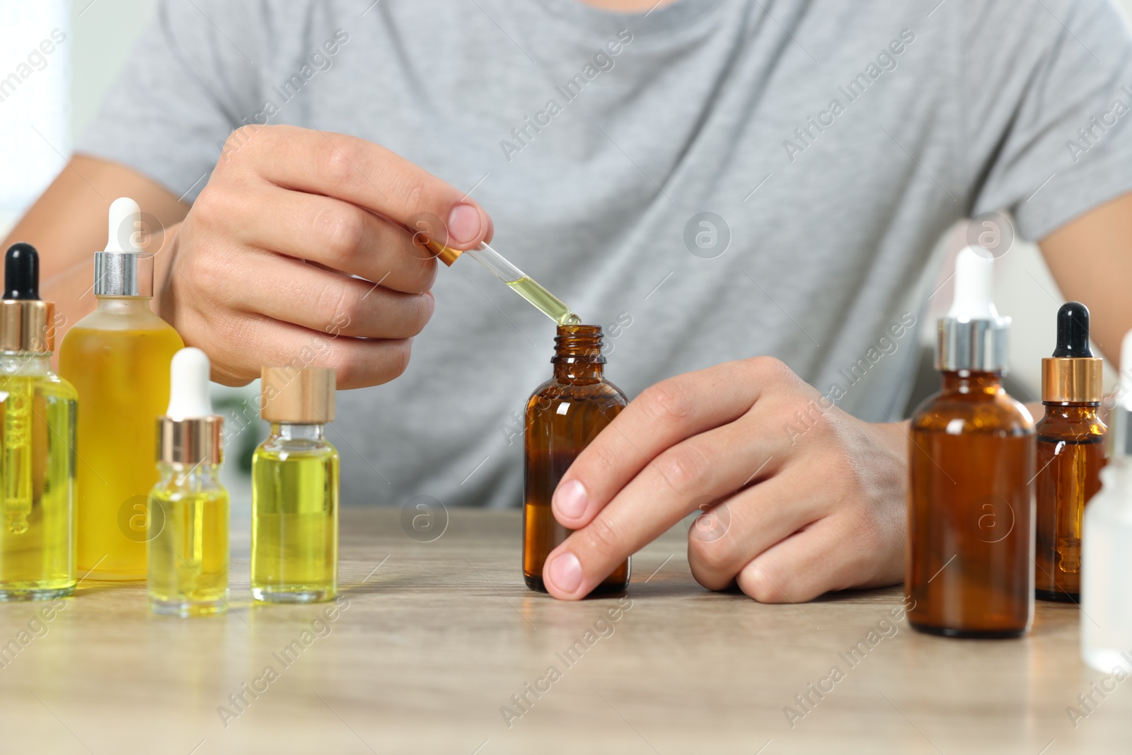 Photo of Young man dripping CBD tincture into bottle from dropper at wooden table, closeup