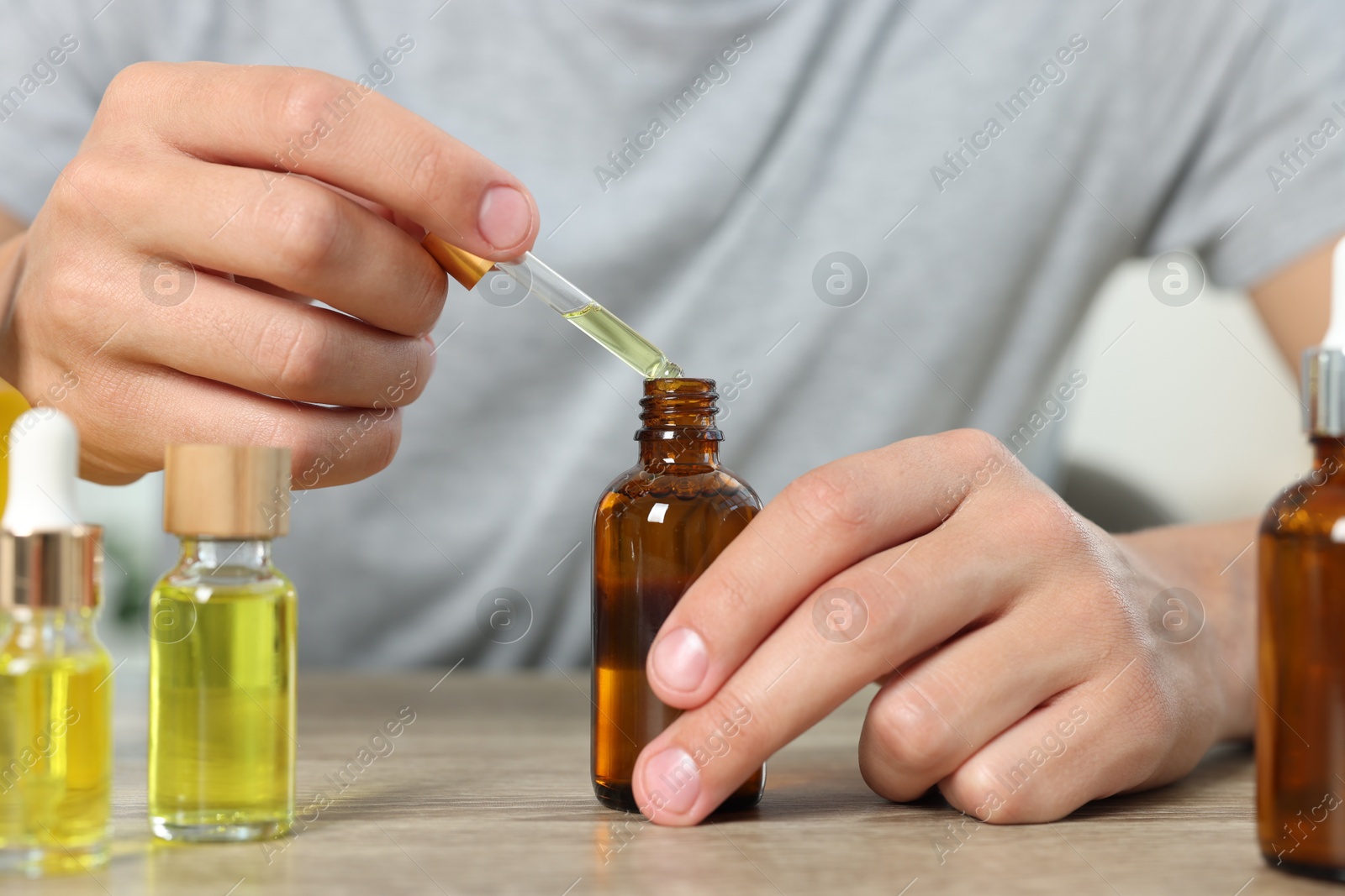 Photo of Young man dripping CBD tincture into bottle from dropper at wooden table, closeup