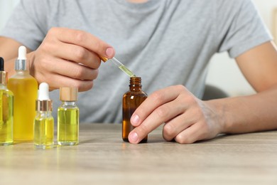 Young man dripping CBD tincture into bottle from dropper at wooden table, closeup