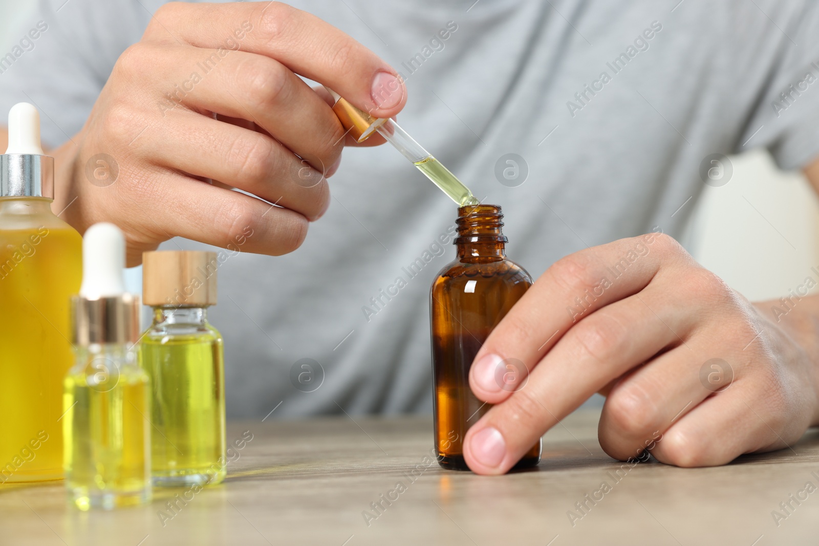 Photo of Young man dripping CBD tincture into bottle from dropper at wooden table, closeup