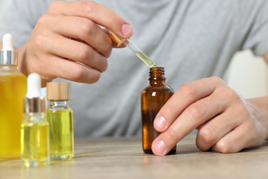 Young man dripping CBD tincture into bottle from dropper at wooden table, closeup