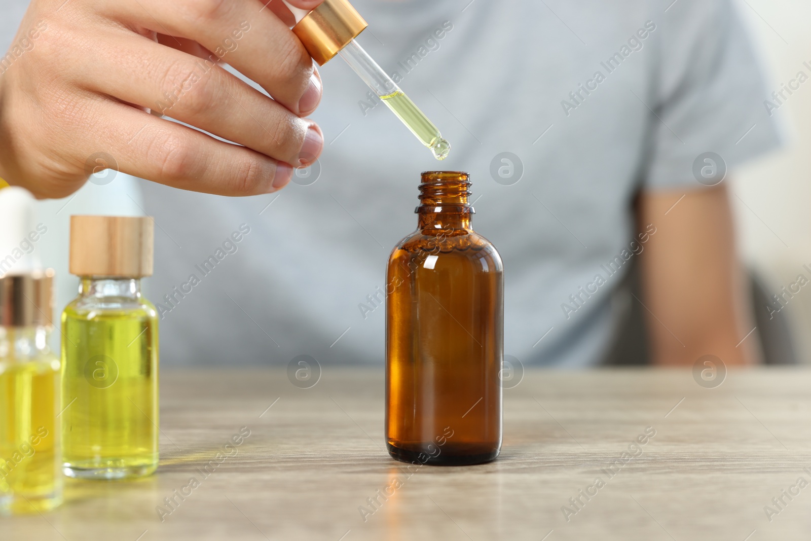 Photo of Young man dripping CBD tincture into bottle from dropper at wooden table, closeup